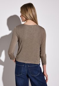 Brun långärmad topp med rundad halsringning och rynkade detaljer på ärmarna, kombinerad med mörkblå jeans som har bakfickor.