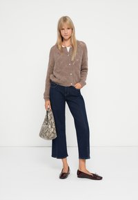 Cardigan maro, texturat, cu nasturi, asortat cu blugi scurți de culoare albastru închis și pantofi lustruiți burgundy. Ținând o geantă gri cu imprimeu de șarpe.