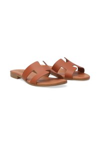 Brown leather sandals featuring a wide, cut-out design, flat sole, open toe, and minimalistic style with light brown accents.