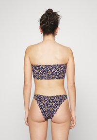 Biquíni floral preto com flores roxas, amarelas e azuis. Top bandeau e parte de baixo com corte atrevido. Tecido suave com detalhes em hardware mínimos.
