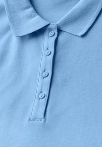 Ljusblå polo t-shirt med en texturerad stickad tyg, klassisk krage och fyra matchande knappar längs placket.