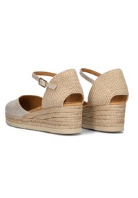 Beige wedge schoenen met een geweven textuur, uitsnede bij de achterhak, enkelband met een gouden gesp en jute-achtige details op de zool.
