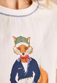 Lühikeste varrukatega kreemivärvi särk, millel on graafika kapuutsiga ja salliga rebane, sinise krae ja tekstuursete detailidega kangal.