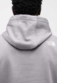 Γκρι φούτερ με μεγάλο καπέλο, με διακριτική υφή και ραφές. Φέρει λευκό λογότυπο στον δεξί ώμο.