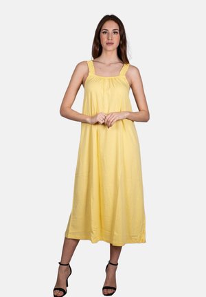 Abito estivo in cotone giallo con scollatura arricciata e spalline arricciate, gonna fluida e orlo al ginocchio, abbinato a tacchi neri con cinturini.