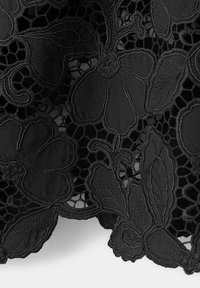 Tissu en dentelle noire avec motifs floraux et détails ajourés, montrant des pétales, des feuilles et des tiges courbées dans un design délicat.