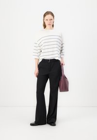 Oversized white sweater with gray stripes, black tailored pants, and a maroon handbag. Black shoes with a textured finish complete the look.