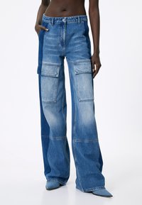 Jeans cargo de pierna ancha hechos de denim. Presenta dos grandes bolsillos frontales, paneles de lavado claro y oscuro, y una cintura alta.