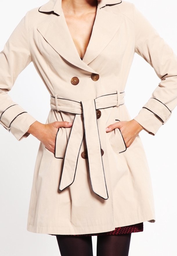 Béžový dvouřadý trench coat s tmavým lemováním, s páskem v pase, bočními kapsami, nošený přes černé punčochy a červenou vzorovanou sukni.