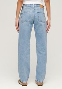 Pantalones vaqueros de mezclilla azul claro, de corte holgado, de cintura alta, con dos bolsillos traseros y una etiqueta de cuero en la cinturilla. Textura deslavada en toda la prenda.