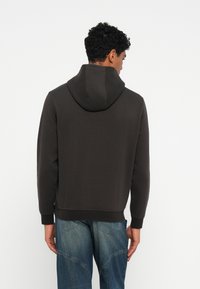 Felpa grigia scura con una texture morbida, dotata di un ampio cappuccio e polsini a costine, abbinata a jeans di denim blu.