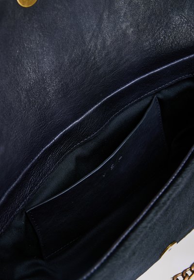 Petit sac en cuir noir ouvert avec une petite poche intérieure et une fermeture par bouton pression en laiton visible.