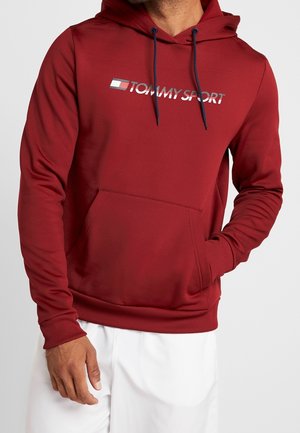 Hoodie rouge avec capuche à cordon et poche avant. Doté d'un grand logo "TOMMY SPORT" en blanc et marine. Texture de tissu lisse.