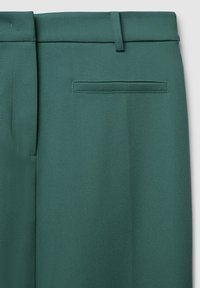 Pantalon vert avec une texture lisse, présentant un devant plat, une taille et une poche arrière unique. Lignes épurées et design ajusté.