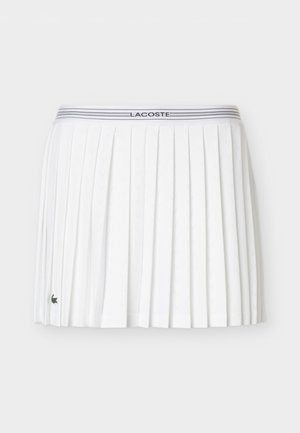 Biała plisowana spódnica z elastycznym pasem w czarne paski i napisem "LACOSTE", oraz małym zielonym logo krokodyla blisko dolnej krawędzi.