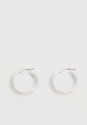 Paire de boucles d'oreilles créoles moyennes argentées brillantes avec de fines attaches métalliques sur un fond clair et neutre.