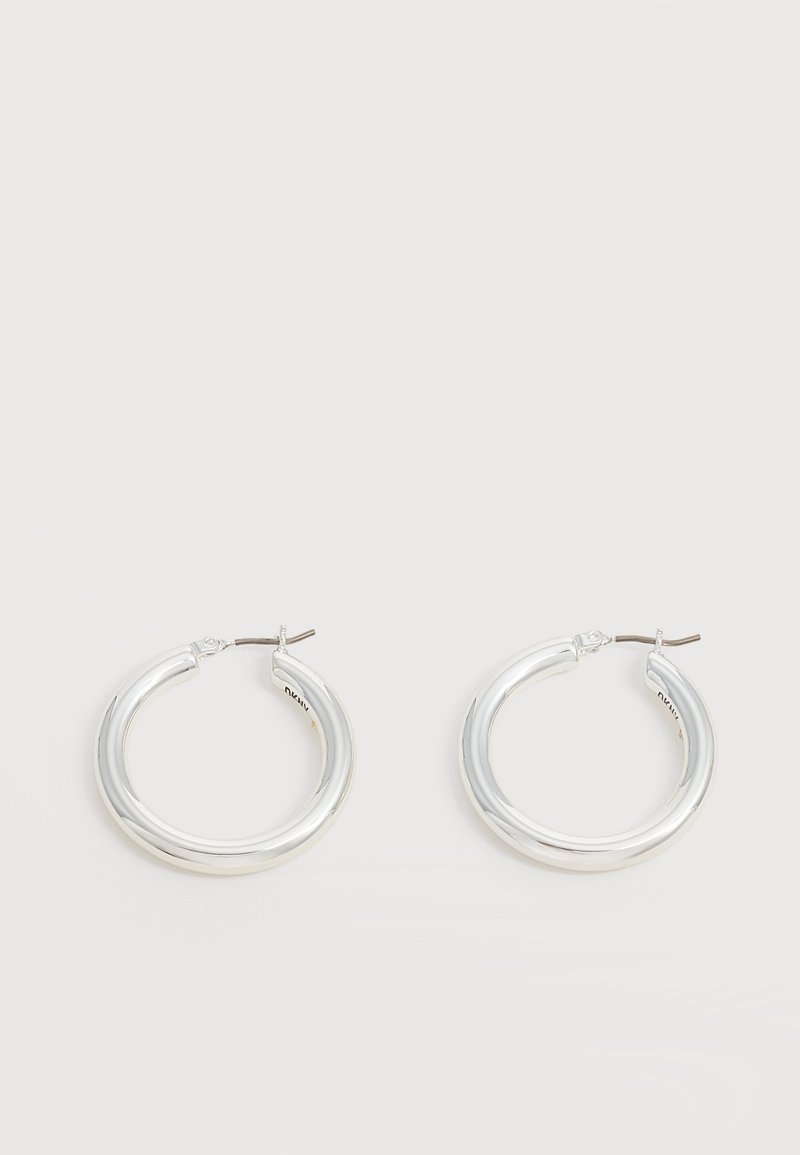 Paire de boucles d'oreilles créoles moyennes argentées brillantes avec de fines attaches métalliques sur un fond clair et neutre.