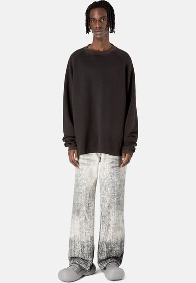 Übergroßes schwarzes Sweatshirt, hellgraue strukturierte, weit geschnittene Hose, graue Slipper. Schlichtes Design mit entspannter Passform und subtilen Details.