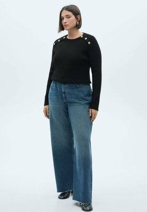 Pull en tricot noir avec des boutons dorés sur les épaules, assorti à un jean en denim bleu à taille haute et jambes larges, et des chaussures noires.