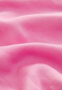 Vaaleanpunainen kangas, jossa on sileä pinta, hieno kudonta ja hienovarainen kiilto, aseteltuna pehmeisiin kaarentoihin, korostaen sen pehmeää pintaa.