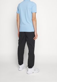 Vaaleansininen lyhythihainen polo-paita mustien housujen kanssa, sisältäen rentoa istuvuutta ja elastiset hihansuut. Valkoiset tennarit täydentävät asun.