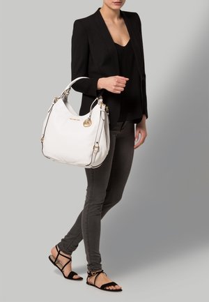 Witte leren handtas met gouden beslag, met een afgeronde vorm, zijstiksels en een afneembare logohanger.