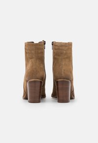 Bottines en cuir suédé marron avec un talon en bois empilé, dotées d'une fermeture éclair à l'arrière et de détails de couture le long de la tige.