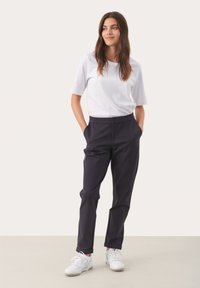 Witte T-shirt met korte mouwen, gecombineerd met donkerblauwe broek. De broek heeft een rechte snit en een knoopsluiting, gedragen met witte sneakers.