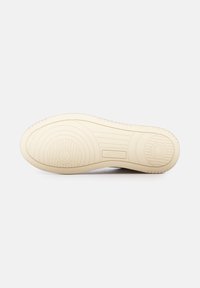 Suola di sneaker bianca con una suola beige strutturata, caratterizzata da motivi circolari e striati. Logo "AUTRY" impresso vicino al tallone.