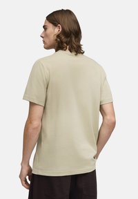 T-shirt à manches courtes et col rond en coton beige clair, avec une coupe décontractée et une texture lisse, vu de dos.