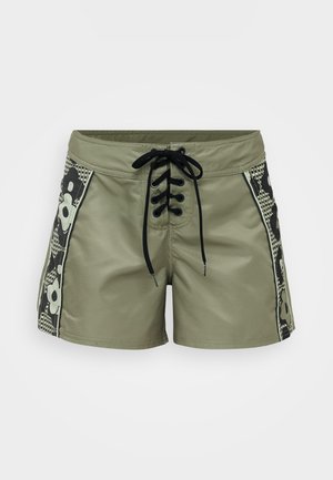 Olive green swim shorts with black lace-up front, patterned side panels featuring floral motifs, and contrasting grid design.