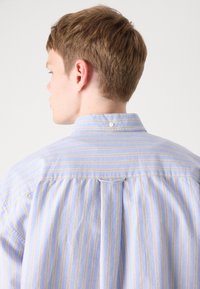 Ανοιχτό μπλε πουκάμισο με ρίγες, διαθέτει κλασικό γιακά, κουμπί στο πίσω μέρος και υφή με κατακόρυφες γραμμές και διακ�ριτικά χρώματα.