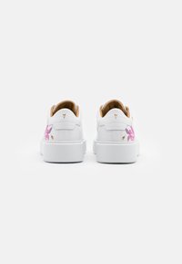 Baskets en cuir blanc à profil bas, ornées de motifs floraux roses sur les côtés et d'une doublure intérieure texturée couleur tan.