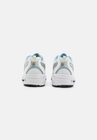 Ett par vita sportskor med ljusblå och grå detaljer, visade bakifrån mot en vit bakgrund.