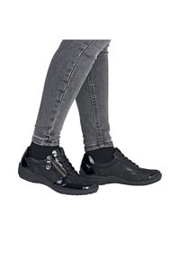 Baskets noires avec une finition brillante en vernis, détail texturé, design à lacets et une fermeture éclair sur le côté. Associées à un jean gris.