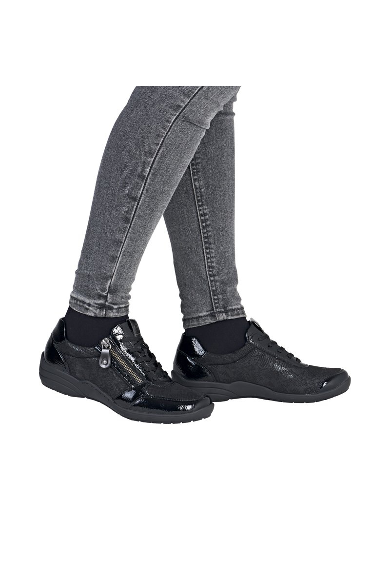 Baskets noires avec une finition brillante en vernis, détail texturé, design à lacets et une fermeture éclair sur le côté. Associées à un jean gris.