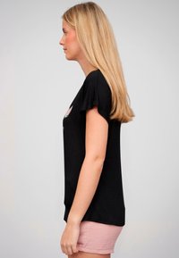T-shirt noir à manches courtes avec un motif floral, associé à un short texturé rose clair. Tissu doux avec une coupe décontractée.