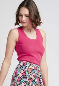 Débardeur en fuchsia à côtes avec des bords festonnés, associé à une jupe à motifs floraux dans des couleurs pastel sur un fond noir.