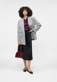 Harmaa kaksirivinen bleiseri burgundin värisen satiinitopin ja mustan laskostetun hameen päällä. Mustat tasapohjakengät ja maroonin värinen käsilaukku viimeistelevät asun.