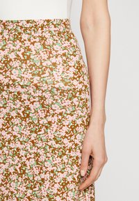 Jupe florale marron, ornée de fleurs roses et vertes. Le tissu est lisse, avec un design ajusté et une taille haute.