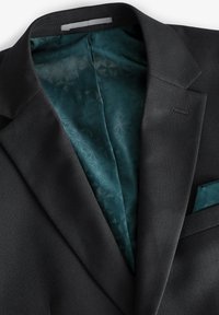 Blazer nero con tessuto strutturato, dotato di fodera verde acqua con motivo e fazzoletto da taschino. Presenta un colletto a risvolto con dettaglio a lapi.