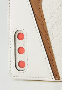 Piele albă texturată cu accente maro embosate, având trei butoane circulare roșii într-o decupare rectangulară.