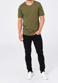 Olivově zelené tričko s krátkým rukávem, kulatým výstřihem, kombinované s černými slim-fit džíny a bílými teniskami. Jednoduchý design, bavlněný materiál.