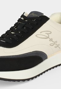 Baskets blanches et noires avec des lacets noirs, des coutures grises et un logo signature sur le côté près du talon et sur la languette.