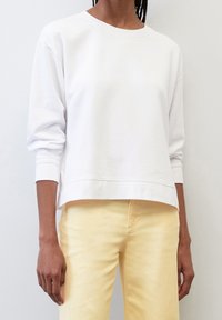 Felpa bianca oversize con maniche lunghe, polsini a costine e scollo tondo. Presenta una vestibilità comoda e una superficie liscia. Abbinata a pantaloni gialli.