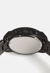 Zwarte roestvrijstalen horloge met een gladde, ronde kast; heeft drie knoppen aan de zijkant en een gestructureerde kroon; gepolijste metalen achterkant.