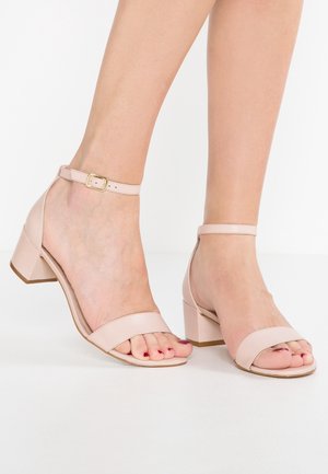 Lichtroze sandalen met blokhak, open teen en een enkelriem met goudkleurige gesp. Gemaakt van glad leer met een minimalistisch ontwerp.