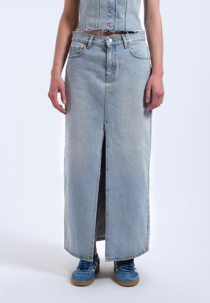 Denimmaxikjol i ljusblått med framslits, med hög midja och fransad fåll. Matchad med blå sneakers för en avslappnad stil.