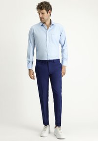 Camicia azzurra a maniche lunghe con bottoni, pantaloni blu navy e sneakers bianche. La camicia presenta una tasca sul petto e polsini regolabili.