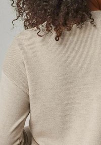 Beiger, strukturierter Pullover mit einem gerippten Strickdesign und breiten Schulternähten. Der Stoff ist weich und hat einen lockeren Schnitt.